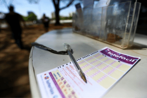 Aposta de Barueri SP acerta Lotofácil 3407, visível com uma caneta sobre o bilhete de apostas ao ar livre, com pessoas ao fundo durante o dia.