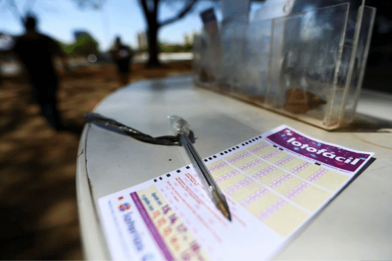 Aposta de Barueri SP acerta Lotofácil 3407, visível com uma caneta sobre o bilhete de apostas ao ar livre, com pessoas ao fundo durante o dia.