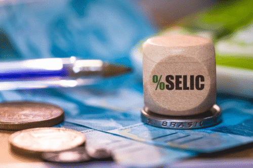 Ilustração com um cubo com escrito Selic sobreposto a uma moeda do Real brasileiro.