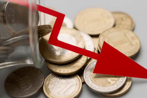Foto de moedas sobrepostas por uma seta que indica queda.