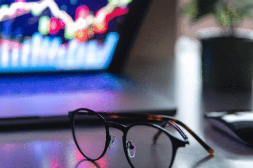 Óculos sobre uma mesa ao lado de um computador que ilustra um gráfico.