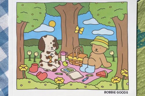 Ilustração do livro Bobbie Goods com um piquenique fofo entre um ursinho e um cachorro em um cenário colorido e alegre.