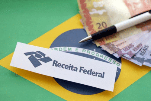 Imagem de um documento do Receita Federal ao lado de notas de dinheiro e uma caneta, simbolizando questões fiscais e tributárias no Brasil.