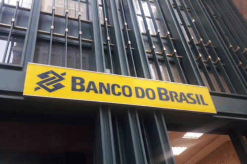 Fachada de uma agência do Banco do Brasil com placa amarela e letreiro em destaque, exibindo a logo e nome do banco.