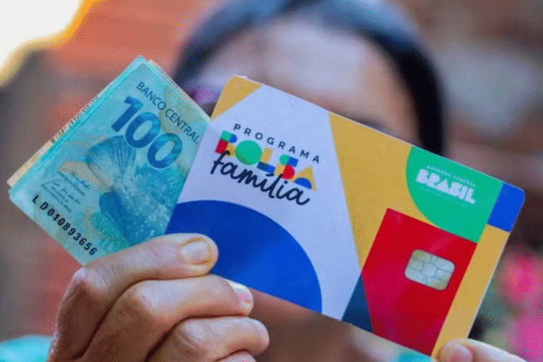 Pessoa segurando um cartão do programa Bolsa Família com dinheiro de 100 reais ao fundo, destacando benefícios sociais no Brasil.