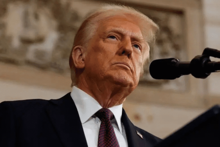 Imagem de Donald Trump durante um discurso, com expressão séria, vestido com terno e gravata, em ambiente formal.