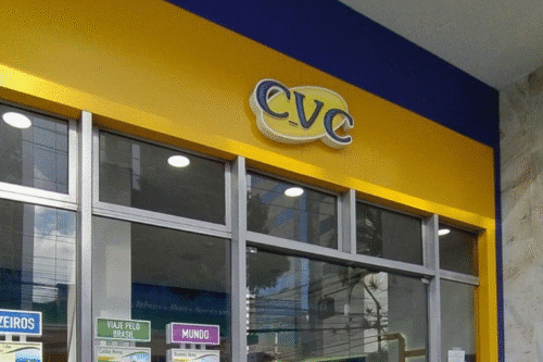 Fachada de uma loja CVC com logo amarelo e azul, destaque para a entrada de vidro e cartazes informativos na frente, localizada no Brasil.