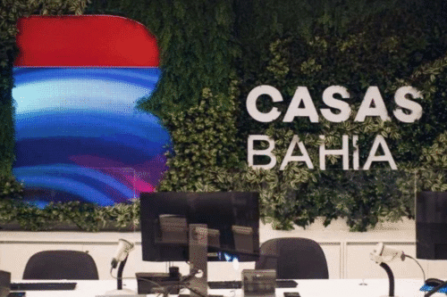 Recepção do espaço Casas Bahia com decoração de parede verde, logo da marca e mobiliário de escritório com computadores e cadeiras.