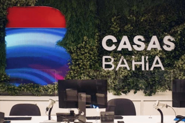 Recepção do espaço Casas Bahia com decoração de parede verde, logo da marca e mobiliário de escritório com computadores e cadeiras.