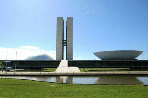 Imagem do Palácio da Alvorada com arquitetura moderna e espaço ao redor, localizado em Brasília, Brasil, sob céu claro e ensolarado.
