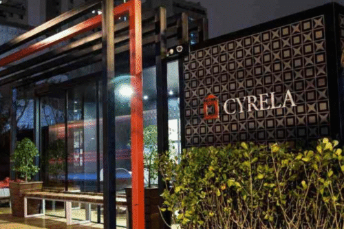 Imagem de fachada de um restaurante chamado Cyrela com design moderno e iluminação noturna, destaque para as plantas na frente e a placa com nome da marca.