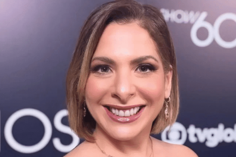 Daniela Lima sorridente com cabelo castanho e maquiagem sofisticada em evento com fundo escuro e logos. Ideal para conteúdo de beleza, eventos e celebridades.