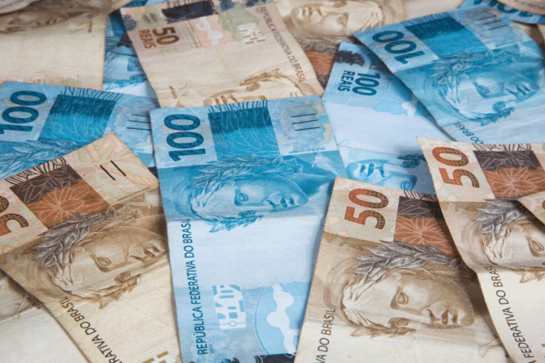 Diversas notas de dinheiro brasileiro, incluindo cédulas de 50, 100 e 200 reais, espalhadas sobre uma superfície, usadas em transações financeiras.