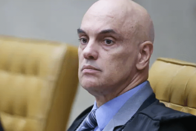 Alexandre de Moraes em tribunal, com expressão séria, usando beca preta e gravata, sentado em uma cadeira de tribunal