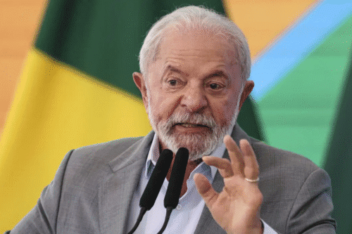 Lula durante discurso político, usando terno cinza, com fundo da bandeira do Brasil, destacando-se pela expressão facial e gestos durante fala.