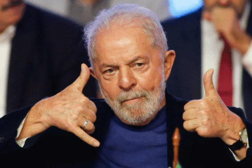Lula, fazendo sinal de telefone com as mãos, em ambiente formal.