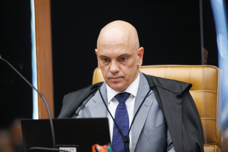 Alexandre de Moraes toga preta e gravata azul trabalhando em tribunal com expressão séria e concentrada.