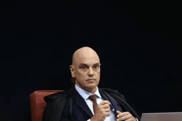 Homem de terno e gravata em ambiente formal, com expressão séria e cabeça raspada, possivelmente em evento ou reunião