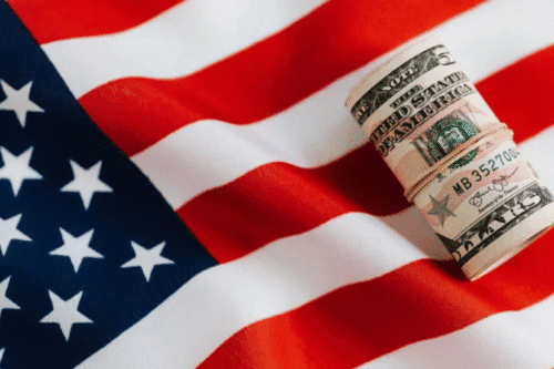 Bandeira dos Estados Unidos com rolo de dinheiro americano em seu centro, representando economia e finanças nos EUA.