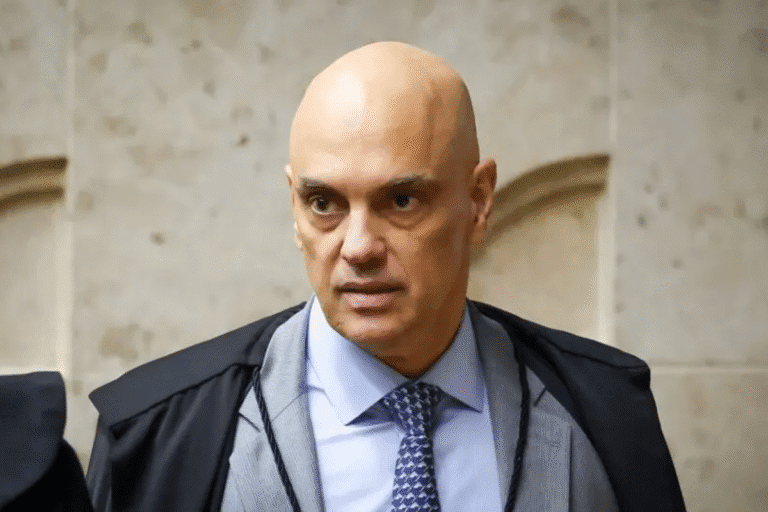 Homem de terno e gravata em ambiente formal, com expressão séria e cabeça raspada, possivelmente em evento ou reunião