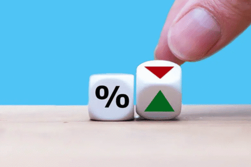 Imagem de dois dados com símbolos de porcentagem e setas vermelha e verde, representando variação de taxas ou juros, com fundo azul claro.