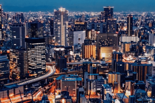Vista noturna de uma cidade moderna com arranha-céus iluminados, ruas movimentadas e skyline urbano de alta densidade, destacando o cenário urbano vibrante.