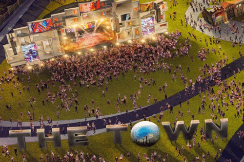 Impressionante vista de uma grande apresentação ao ar livre na arena de The Town, com muitas pessoas assistindo a show e iluminação vibrante.