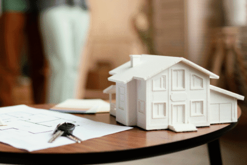 Maquete de uma casa residencial construída em material branco, placements para janelas e portas, sobre uma mesa com documentos e chaves, em ambiente de escritório de arquitetura.