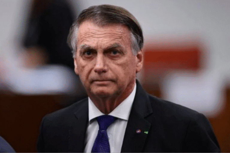 Imagem do ex-presidente Jair Bolsonaro com expressão séria, usando terno e gravata, em ambiente formal com fundo desfocado.