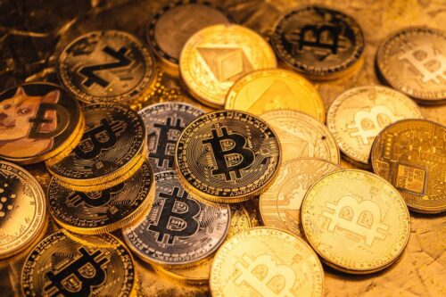Imagem com diversas moedas físicas representando criptomoedas para investir, incluindo Bitcoin, Ethereum e Dogecoin.