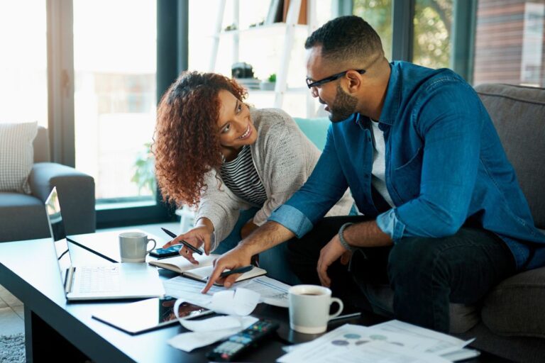 Casal analisando documentos e laptop enquanto organiza o orçamento familiar em casa.