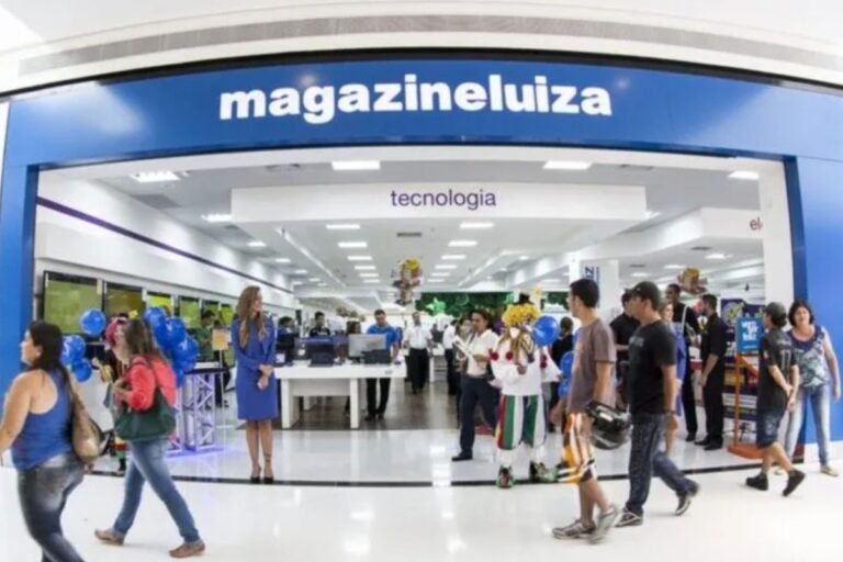 Pessoa entrando na loja MagazineLuiza especializada em tecnologia, com clientes e funcionários dentro e fora do estabelecimento, decorado com balões e sinalização azul.