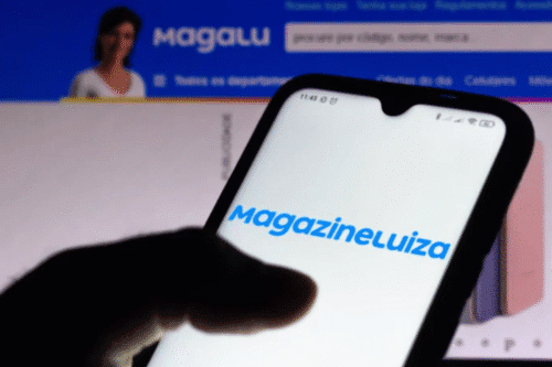 Pessoa segura celular exibindo o logo da Magazine Luiza, com o site da empresa aberto ao fundo.