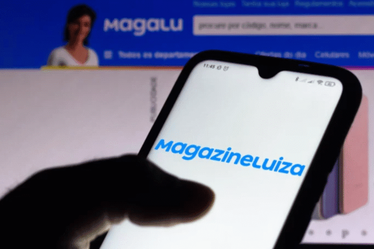 Pessoa segura celular exibindo o logo da Magazine Luiza, com o site da empresa aberto ao fundo.