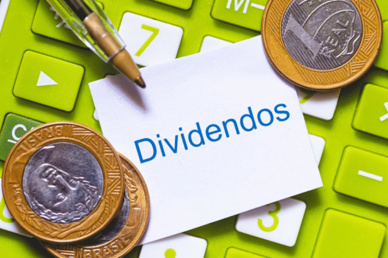 Imagem de moedas e teclado com uma nota escrita 'Dividendos', simbolizando retorno financeiro de investimentos ao lado de uma calculadora.