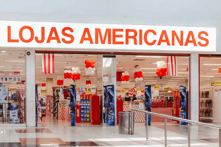 Entrada da loja americanas com decoração de balões nas cores vermelho, branco e laranja, na fachada com destaque para o nome Lojas Americanas.