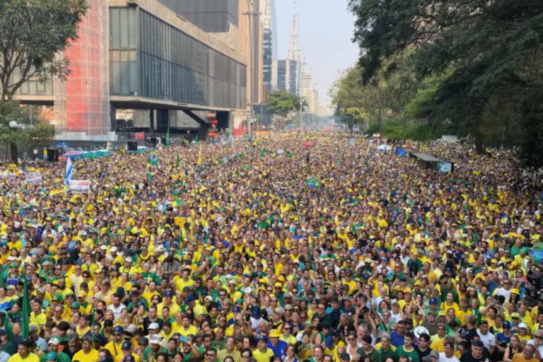 Multidão de pessoas usando roupas amarelas e verdes durante um grande protesto ou evento ao ar livre na cidade, com edifícios modernos ao fundo.