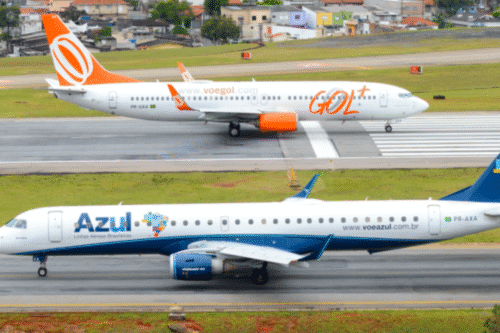 Aeronaves da Gol e da Azul no aeroporto durante o pouso, com destaque para o avião da Gol com cores laranja e logo visível na imagem.