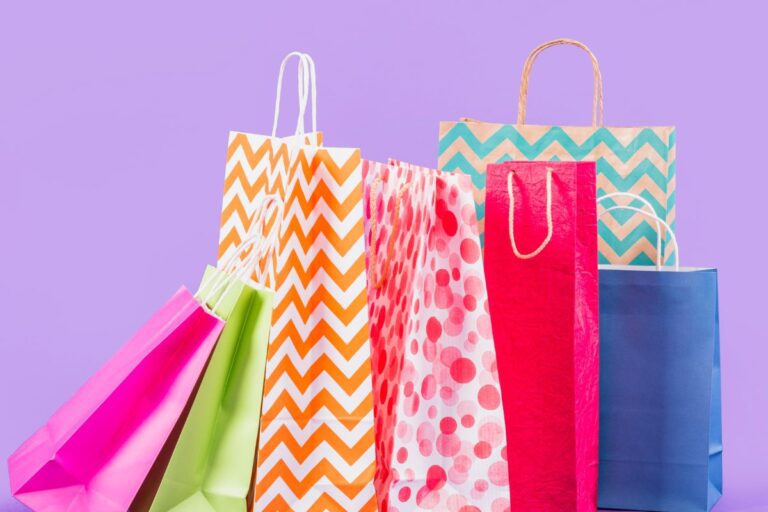 Várias sacolas de compras coloridas em fundo roxo, destacando variedade de cores e padrões, ideal para compras, festas e presentes