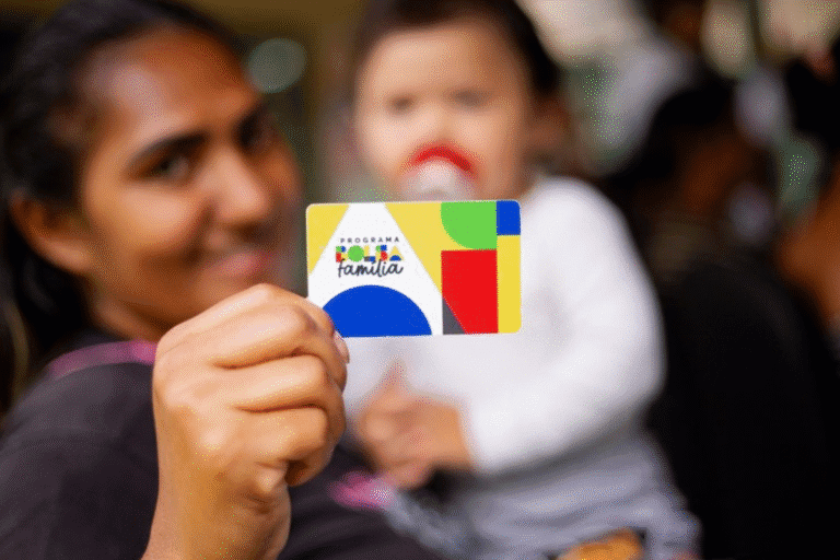 Pessoa segurando cartão do programa 'Famiília Família' em evento, com outras pessoas ao fundo, em um ambiente social e alegre.