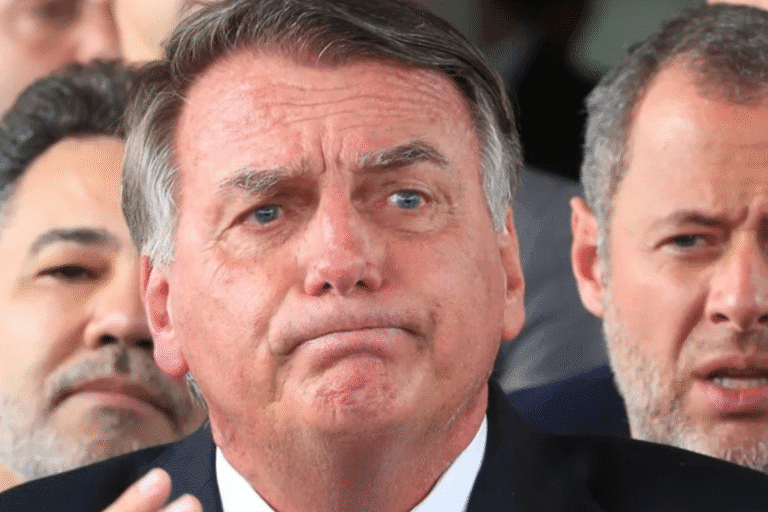 Bolsonaro de terno com expressão facial de dúvida ou preocupação, cercado por outras pessoas ao fundo.