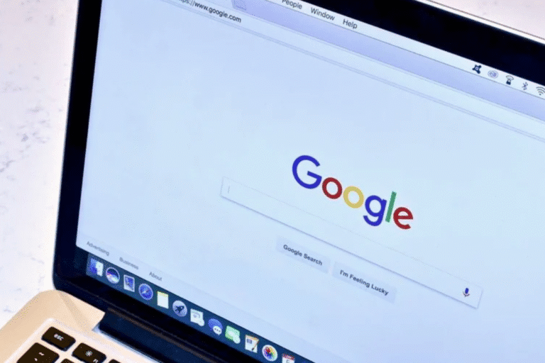 Tela de computador exibindo a página inicial do Google, com o logotipo colorido no centro da tela. Ao lado, uma parte do teclado do computador portátil.