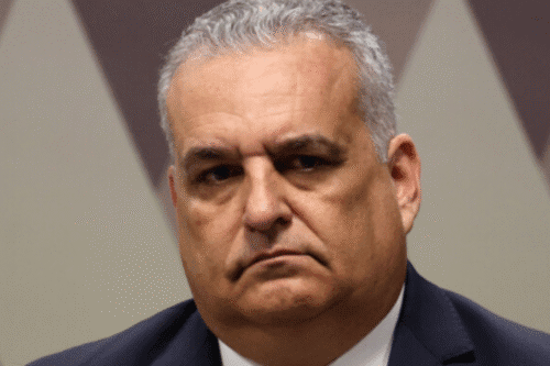 Imagem de um homem sério com cabelo cinza, expressão facial fechada e vestindo terno escuro, em fundo neutro, ideal para conteúdo de negócios e liderança.