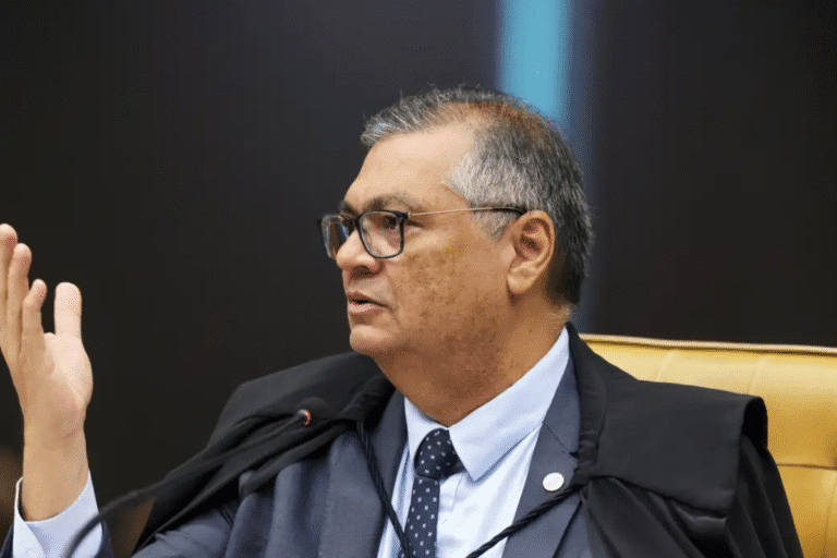 Flávio Dino em uma sessão judicial, vestindo toga e gravata, com expressão séria e gesticulando durante o depoimento ou audiência "juiz de direito".