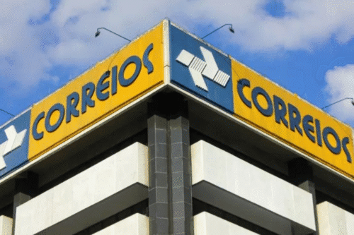Imagem de uma agência dos Correios em um edifício alto, com sinais de entrega postal e o logotipo do Correios visível na fachada.