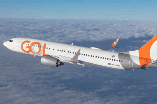 Avião da GOL Linhas Aéreas em voo alto, sobre nuvens, com design moderno em tons de branco, cinza e laranja, destacando a marca GOL na lateral.
