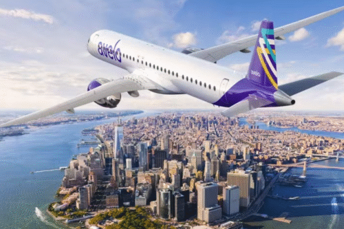 Avião da companhia Avelo Airlines sobrevoando a cidade de Nova York com vista para o rio Hudson, prédios e a ponte do Brooklyn ao fundo, durante voo de cruzeiro.