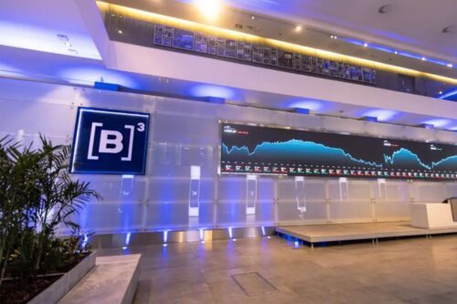 Imagem de um centro de operações financeiras com uma tela exibindo gráficos de mercado e uma decoração moderna com iluminação azul e detalhes em cinza.