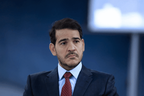 Jorge Messias de terno e gravata vermelha olha pensativo para o lado. Ele tem cabelo curto e escuro e barba aparada. O fundo está desfocado, criando um tom profissional.