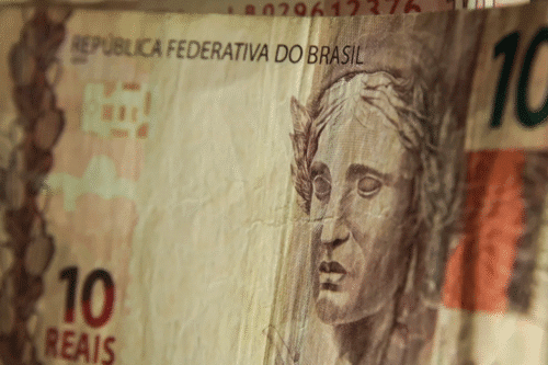 Close de uma nota de 10 reais com um rosto esculpido em relevo. O texto diz "República Federativa do Brasil".